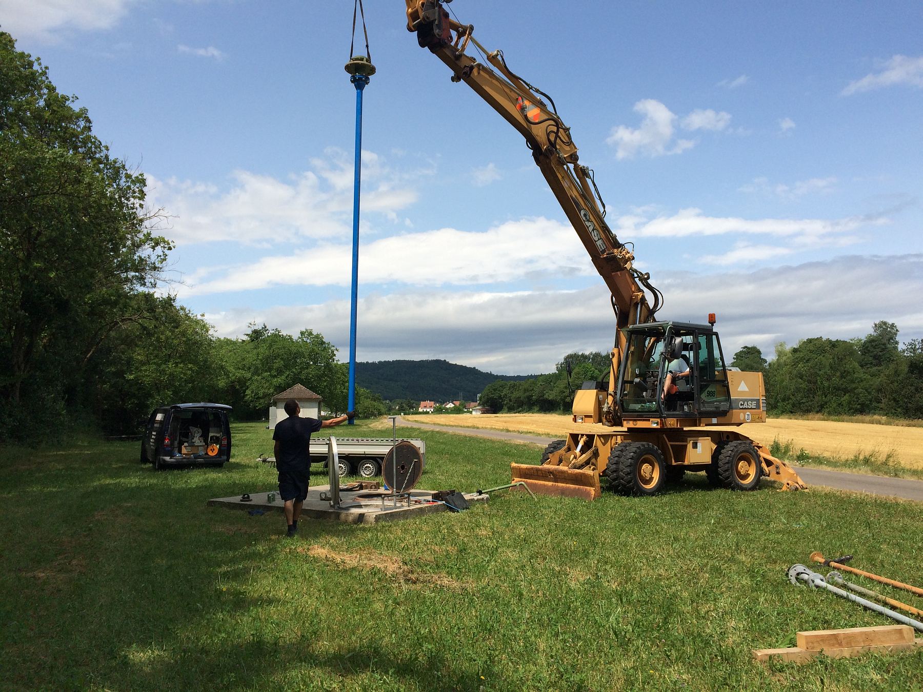 Bagger hebt blaue Tiefbrunnenpumpe bei Montage auf freiem Feld &ndash; Arbeiten zur Grundwassererschlie&szlig;ung