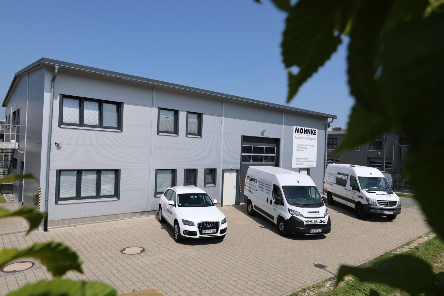 Unternehmensgeb&auml;ude der MOHNKE Wassertechnik & Anlagenbau GmbH in V&ouml;rstetten mit Firmenfahrzeugen &ndash; Kompetenzzentrum f&uuml;r Planung, Beratung und Ausf&uuml;hrung.